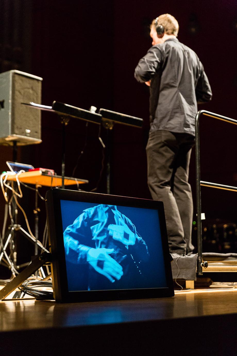 Dirigent von hinten. Von Vorne sieht man auf einem Bildschirm die Verkabelung an den Händen.