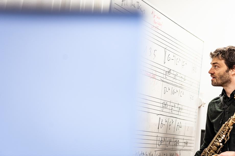 Saxophonprofessor Christian Weidner vor einem Whiteboard, auf dem diverse Akkordfolgen handschriftlich notiert sind.