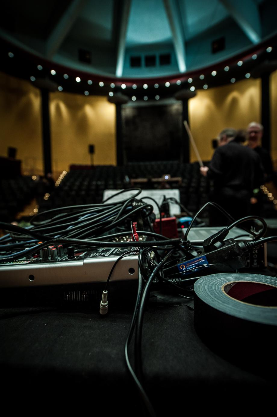 Ein mit Kabeln überdecktes Mischpult. Der Blick geht von der Bühne in den leeren Zuschauerraum des Konzertsaales.