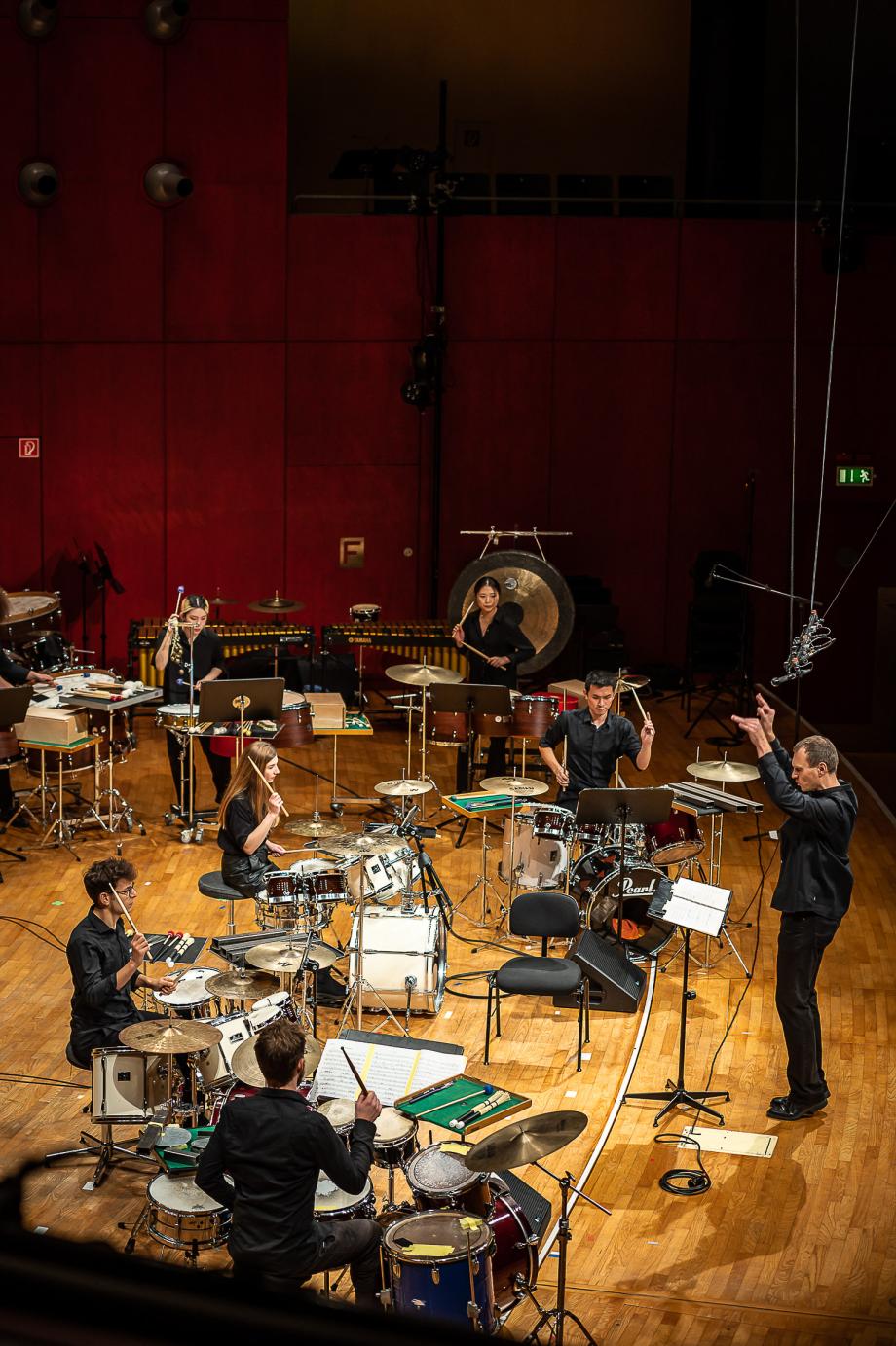 Studierende an unterschiedlichen Schlagwerken auf der Bühne, dirigiert von Christof M Löser.