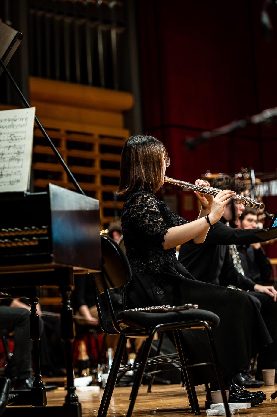 Querflötistin von der Seite portraitiert. Im Hintergrund sind Mitglieder einer Kammerensembles erkennbar.