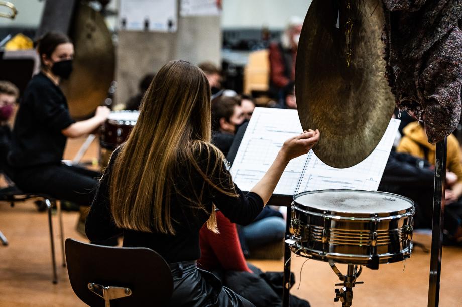 Von hinten beobachtete Schlagzeugstudentin, die mit der rechten Hand ein aufgehängtes Becken berührt.