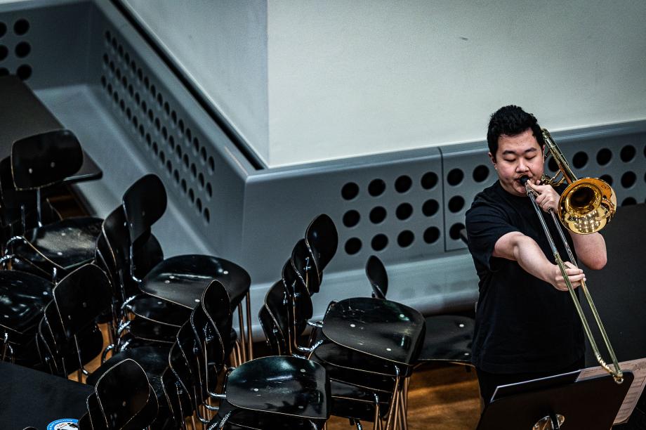 Posaunist, der neben verschiedenen Stuhlstapeln in der Mensa konzertiert.