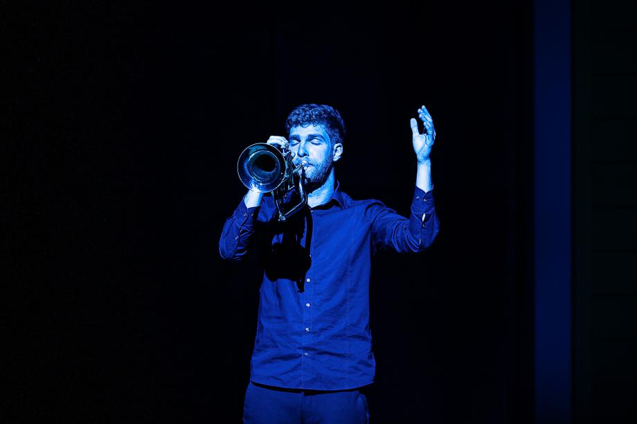 Musizierende Trompeter auf dem Podium, der mit geschlossenen Augen und mit linker erhobener Hand musiziert.