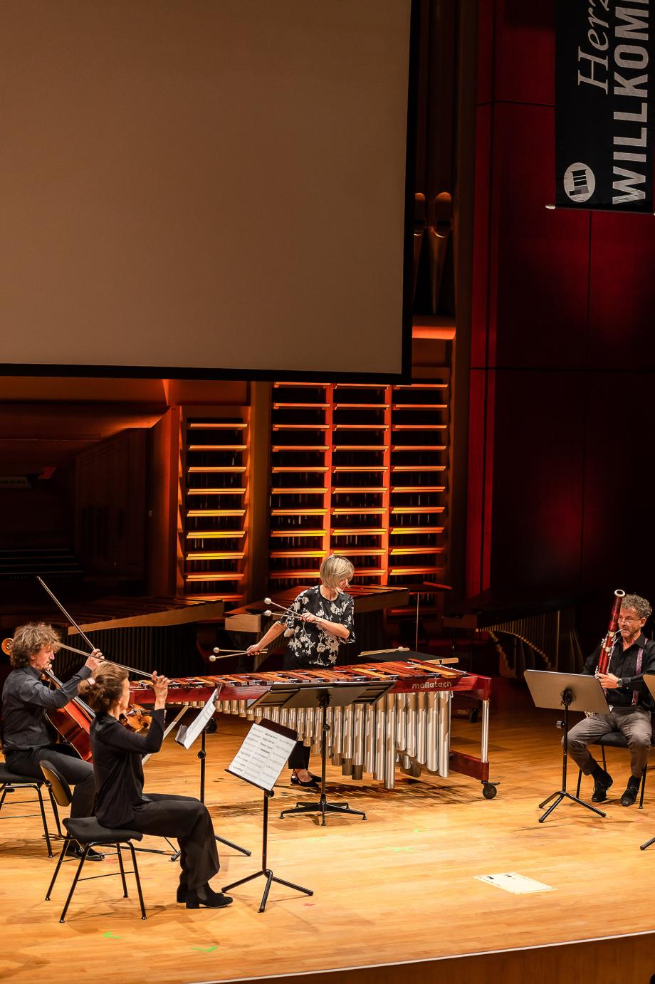 SChlagzeugprofessorin Marta Klimasara auf dem marimbaphon musizierend, umgeben von einer Kammermusikformation von Lehrenden und Studierenden der HMDK.