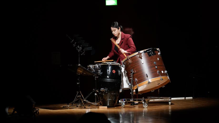 SChlagzeugstudentin mit einem Setup aus Bongos und großer Trommel auf dem Konzertsaalpodium.