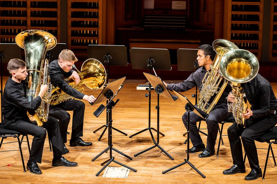 Musizierendes Tubaquartett auf dem Podium. Jeweils zwei Studierende sind sich zugewandt.