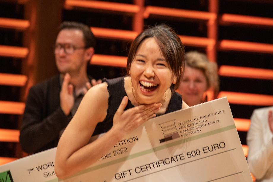 Lachende Sschlagzeugstudentin, die mit einem Preisscheck für ihre Leistung beim Marimbawettbewerb ausgezeichnet wird.