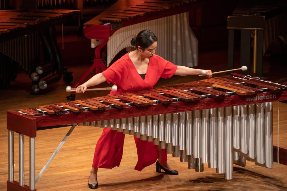 Schlagzeugstudierende mit weit ausgestreckten Armen vor einem Marimbaphon.