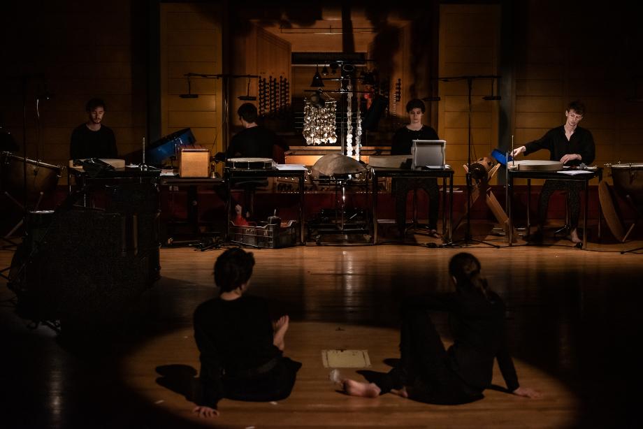 Im Vordergrund sitzen zwei Studierende auf der dunklen Bühneknate, Studierende der Schlagzeugklasse zugewandt. Ein umfangreicher Schlagzeugaufbau breitet sich vor dem Orgelprospekt über die Bühnenbreite aus.