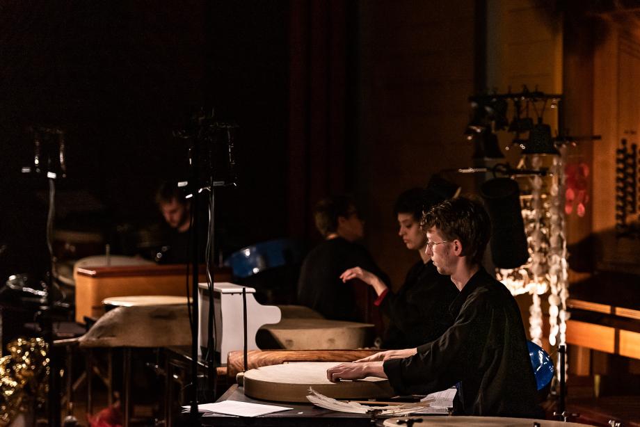 Profiaufnahme von der linken Bühnenkante auf den Schlagzeugaufbau und die musizierenden Studierenden.