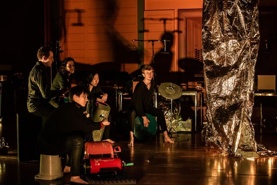 Fünf Schlagzeugstudierende auf der linken Seite des Podiums. In der Mitte ist eine silberne Alufoliensäule aufgebaut.