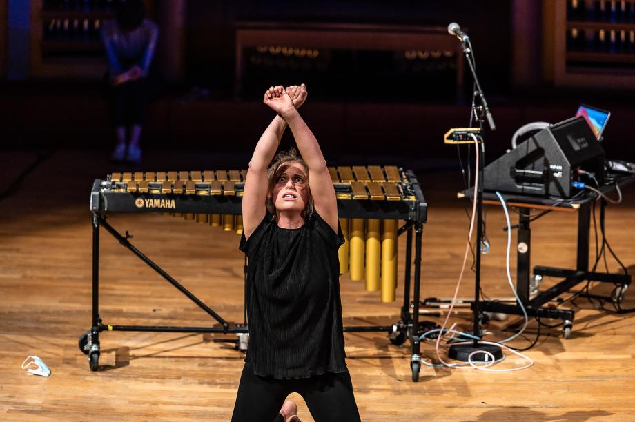 Vanessa Porter kniet auf dem Podium, die Hände nach oben gestreckt. Die beiden Handballen überkreuzt. Ihr Gesichtsausdruck geht verängstigt und leer in den Raum.