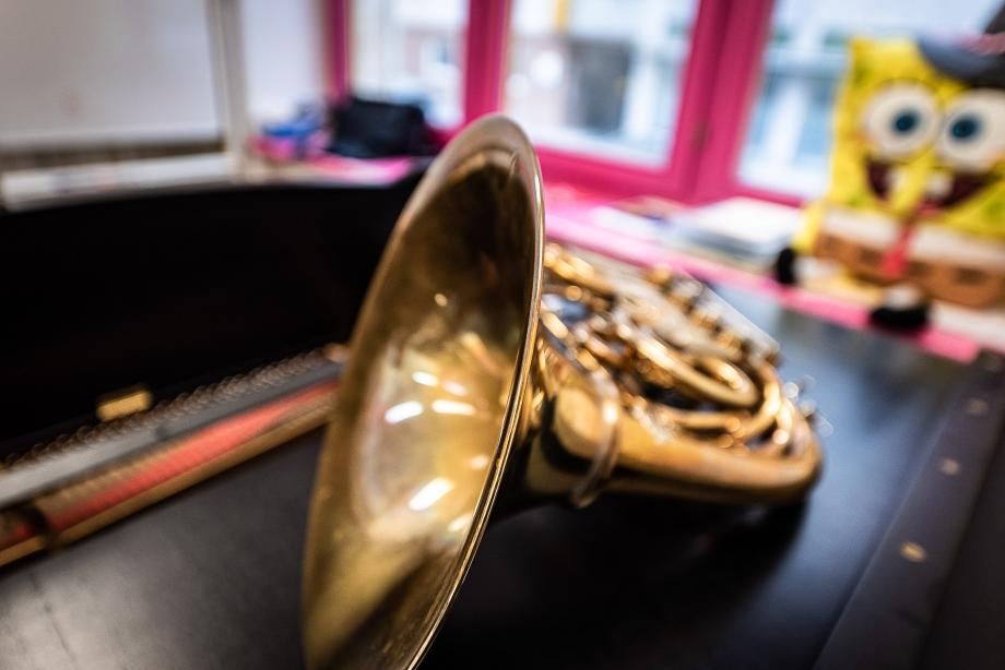 Detailaufnahme eines Hornes, was auf einem schwarzen Sideboard in einem Unterrichtsraum abgelegt ist. Im Hintergrund ist neben dem pinken Fensterrahmen eine große Spongebob-Figur zu erkennen.