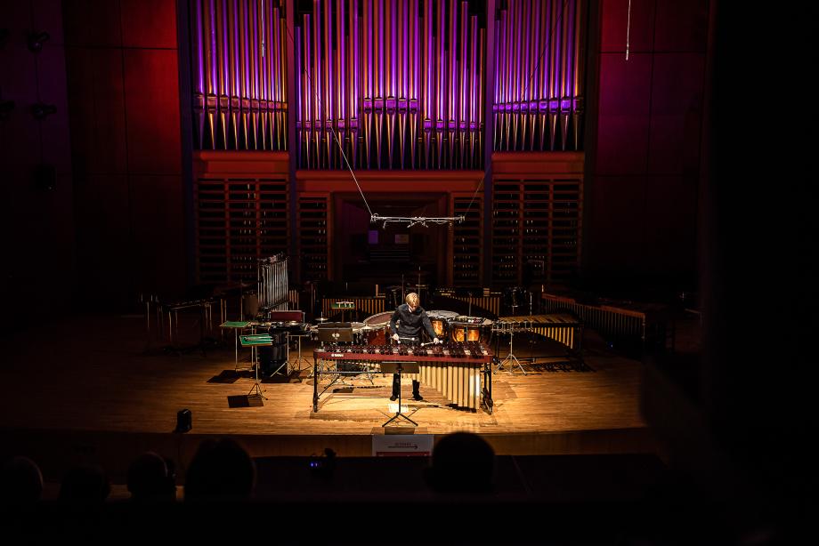 Zentraler Blick aus der Mitte des Zuschauerraumes auf einen Marimba spielenden Studenten. Umrahmt wird er von einem umfangreichen Schlagzeugaufbau mit vielfälltigen Instrumenten.