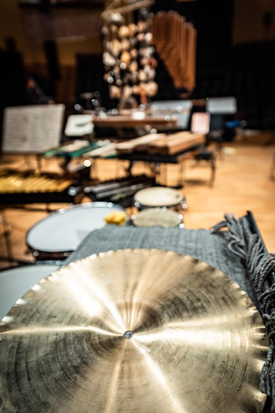 Nahaufnahme von einem Schlagzeugbecken. Dahinter ist verschwommen ein umfangreiches Schlagwerk zu sehen.