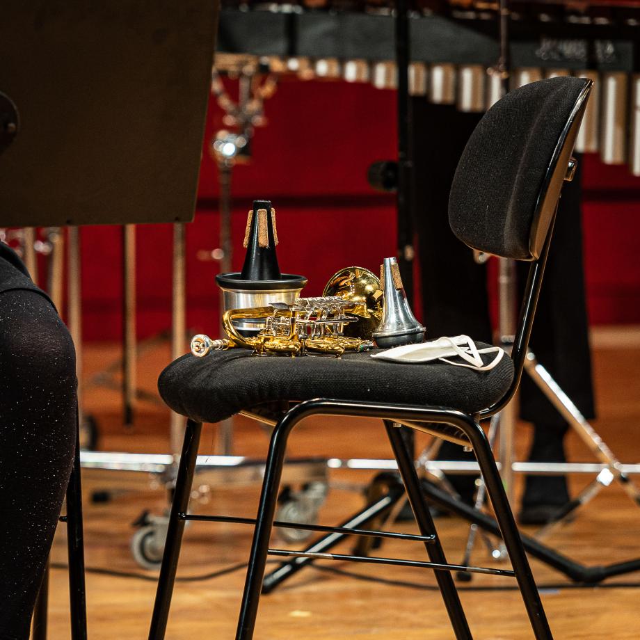 Detailaufnahme einer Trompete auf einem schwarzen Orchesterstuhl mit zwei Dämpfern und einer Gesichtsmaske.