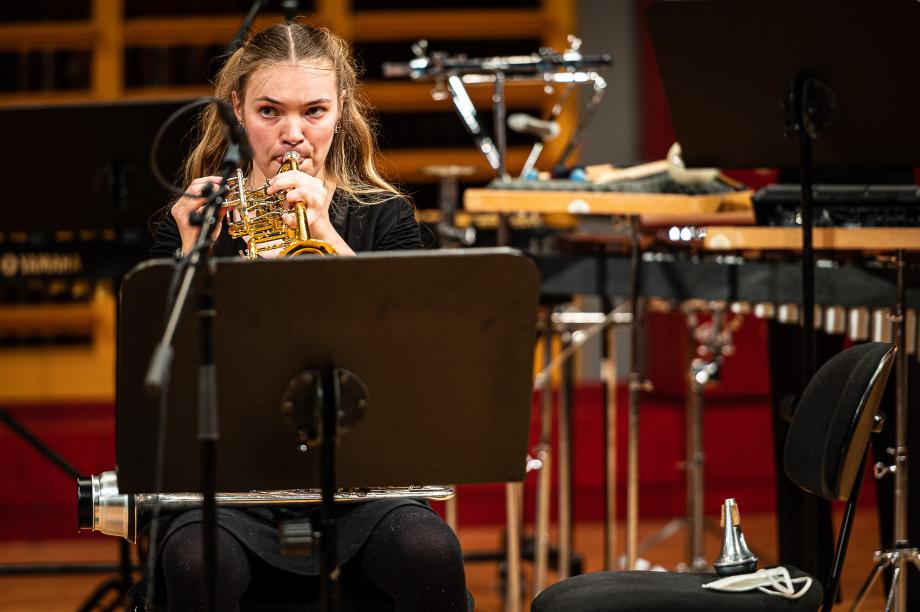 Detailaufnahme einer Trompeterin, die durch ihre Augenausrichtung mit dem Dirigenten verbunden ist.