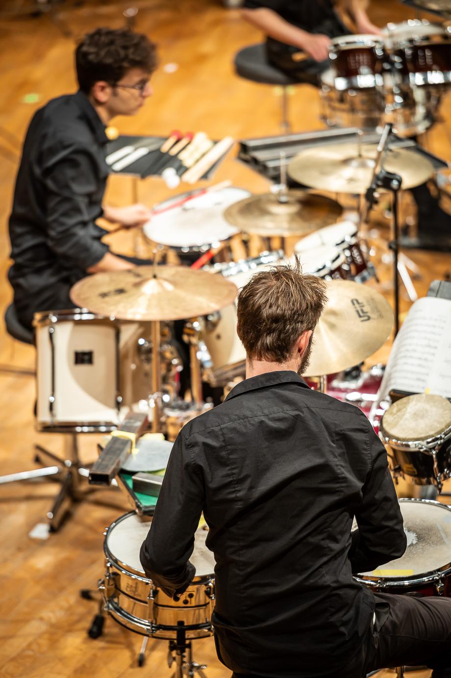 Seitlicher Blick auf Studierende der Schlagzeugklasse vor ihren unterschiedlich großen Setups.