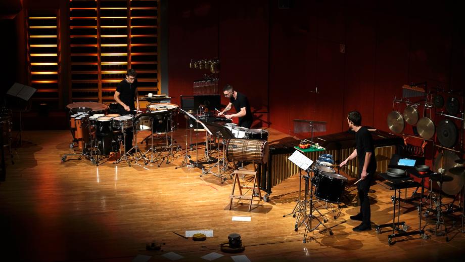 Schlagzeugstudierende mit drei unterschiedlich aufgebauten Setups auf dem Konzertsaalpodium.