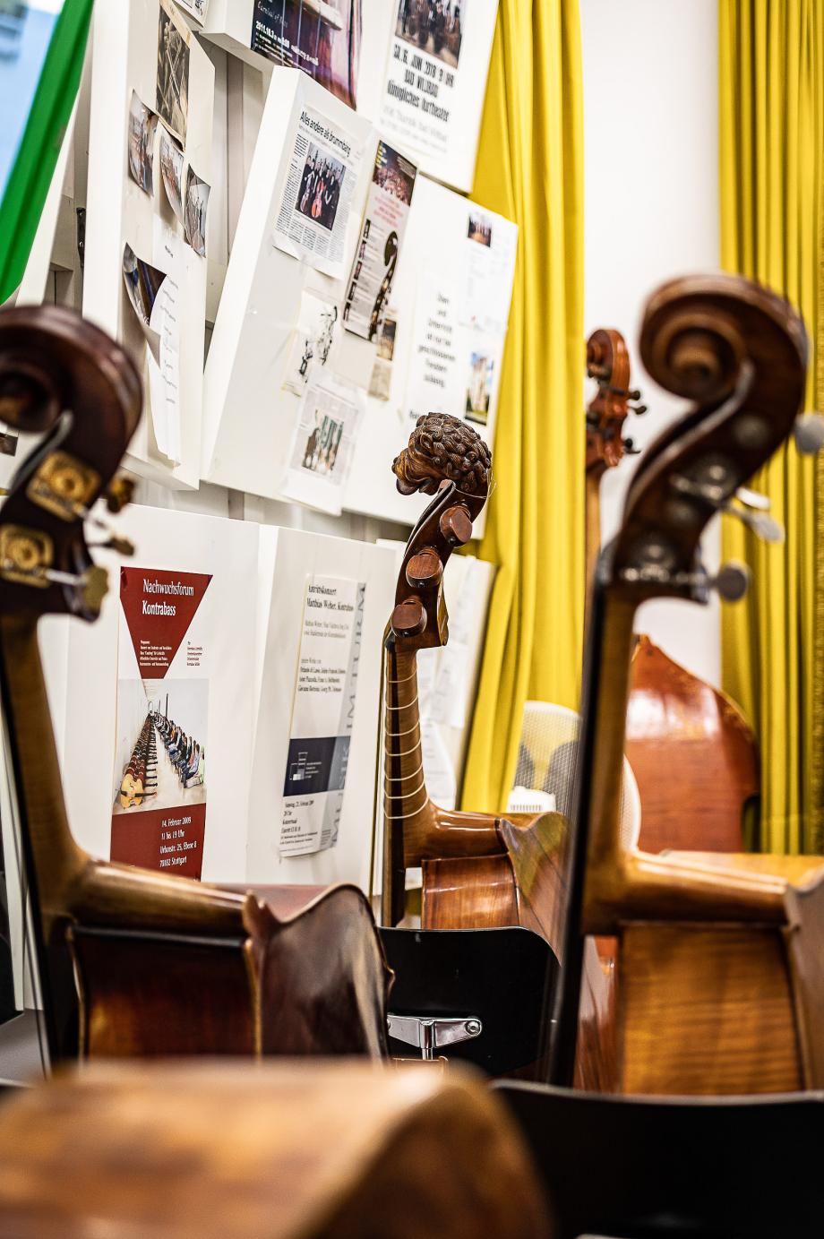 Blick in das Kontrasbasszimmer. Fünf Kontrabässe mit unterschiedlichen Griffbrettern sind an Stühle angelehnt.