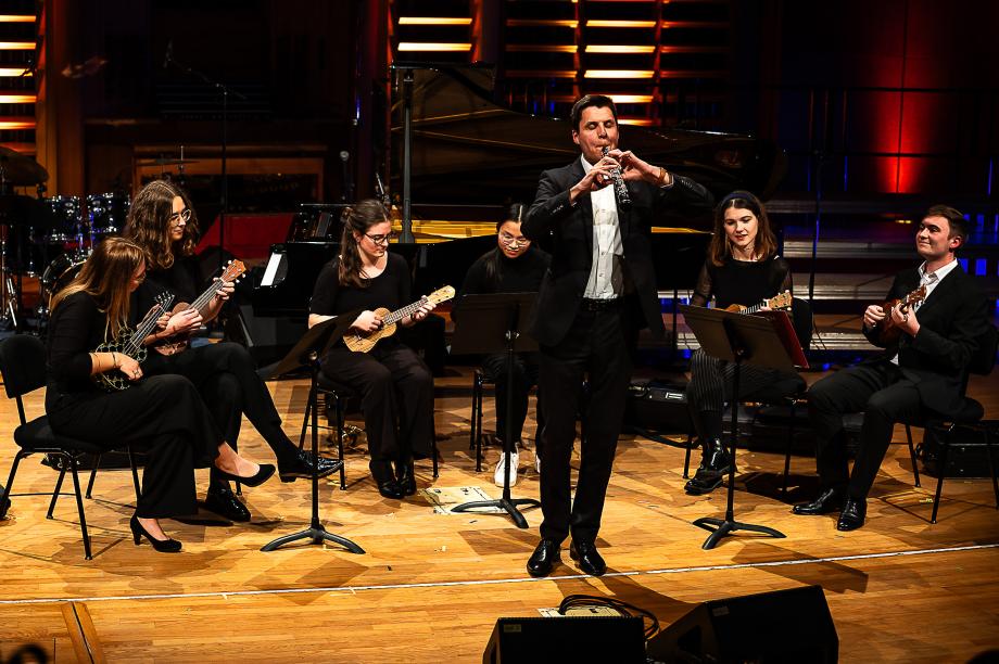 Ukulele-Sextett mit Solokrainettist. Die Ukulele spielenden Studierenden umgeben den Solisten im Halbkreis.