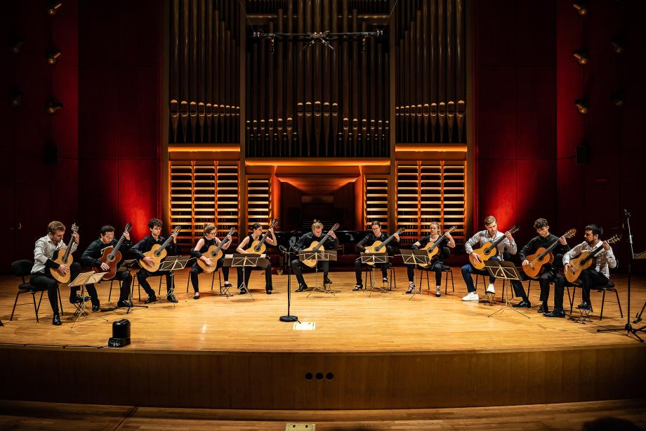 Dreizehnköpfiges Gitarrenensemble bei der La Noche de la Guitarra. Das Ensemble sitzt über die gesamte Bühnenbreite im Halbkreis.