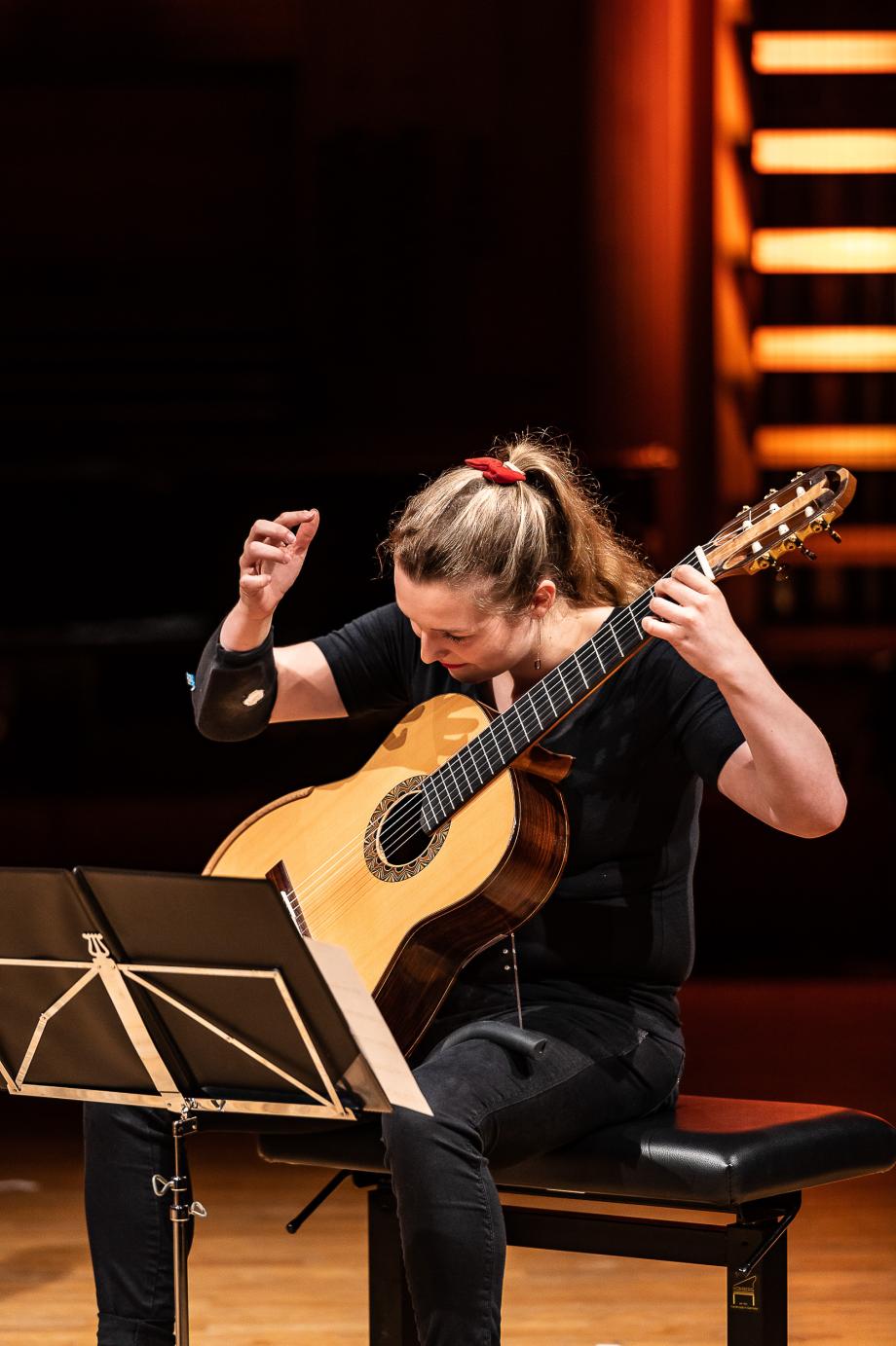 Gitarristin auf dem Konzertpodium. Der rechte Arm geht schwungvoll am Resonanzkörper der Gitarre vorbei.