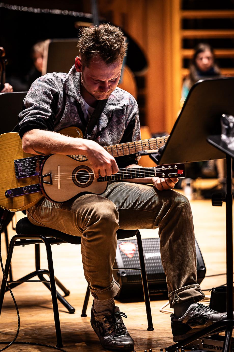E-Bass und Ukulele spielender Studierender. Am Beiden sind Effektgeräte zu erkennen, die durch silberfarbene Sneaker bedient werden.