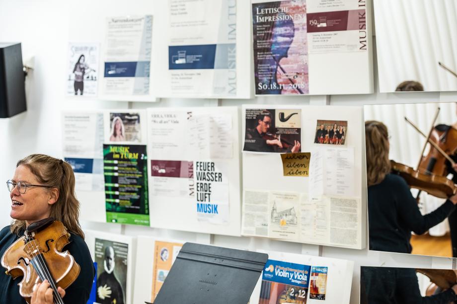 Violaprofessorin Andra Darzins beim Unterrichten. Im Hintergrund sind die Akustikpanels mit Konzertplakaten, Programmzetteln und Bildern beklebt.