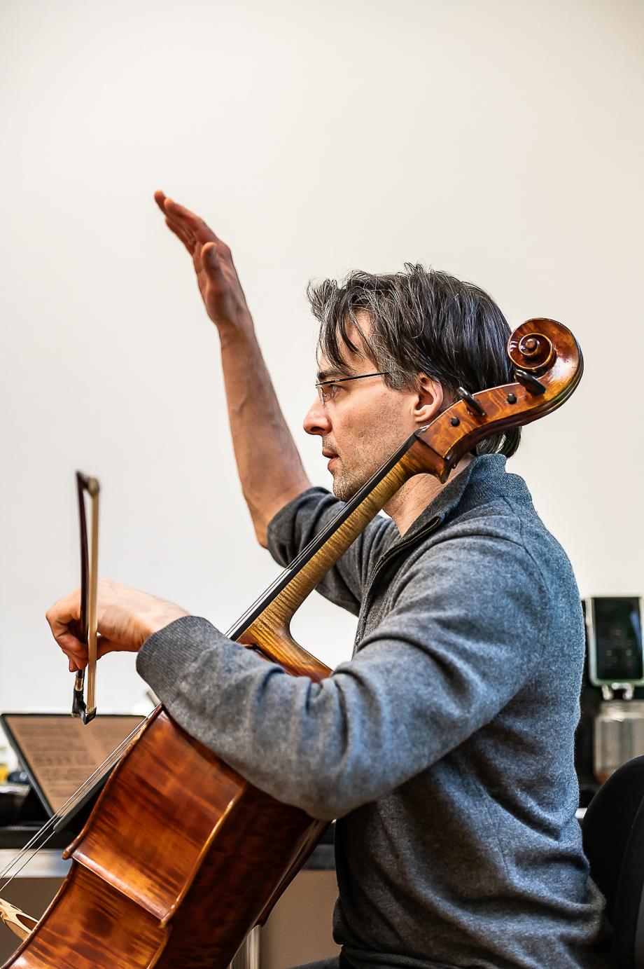 Profilansicht des Violoncelloprofessors Tristan Cornut. Sein rechter Arm ist nach oben gerichtet. Der linke Arm hält den Cellobogen.