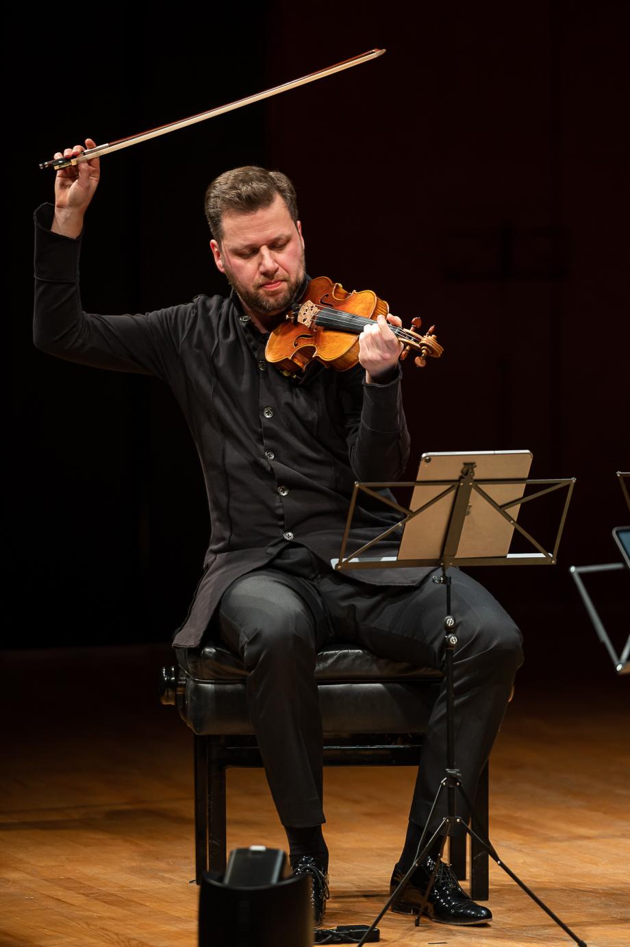 Violinprofessor Martin Funda sitzend auf dem Konzertsaalpodium. 