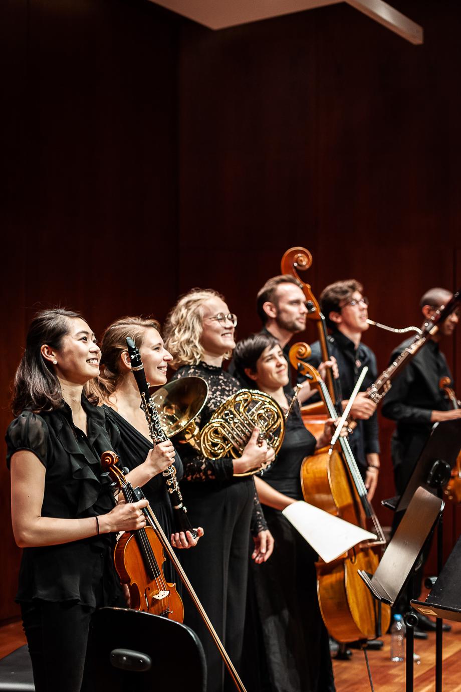 Kammerensemble beim Schlussapplaus in einer Reihe stehend. Die Musikerinnen und Musiker lächeln ins Publikum.