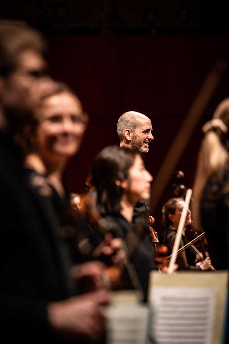 Prof. Rasmus Baumann und Mitgliedes des Hochschulsinfonieorchesters stehend beim Schlussapplaus.