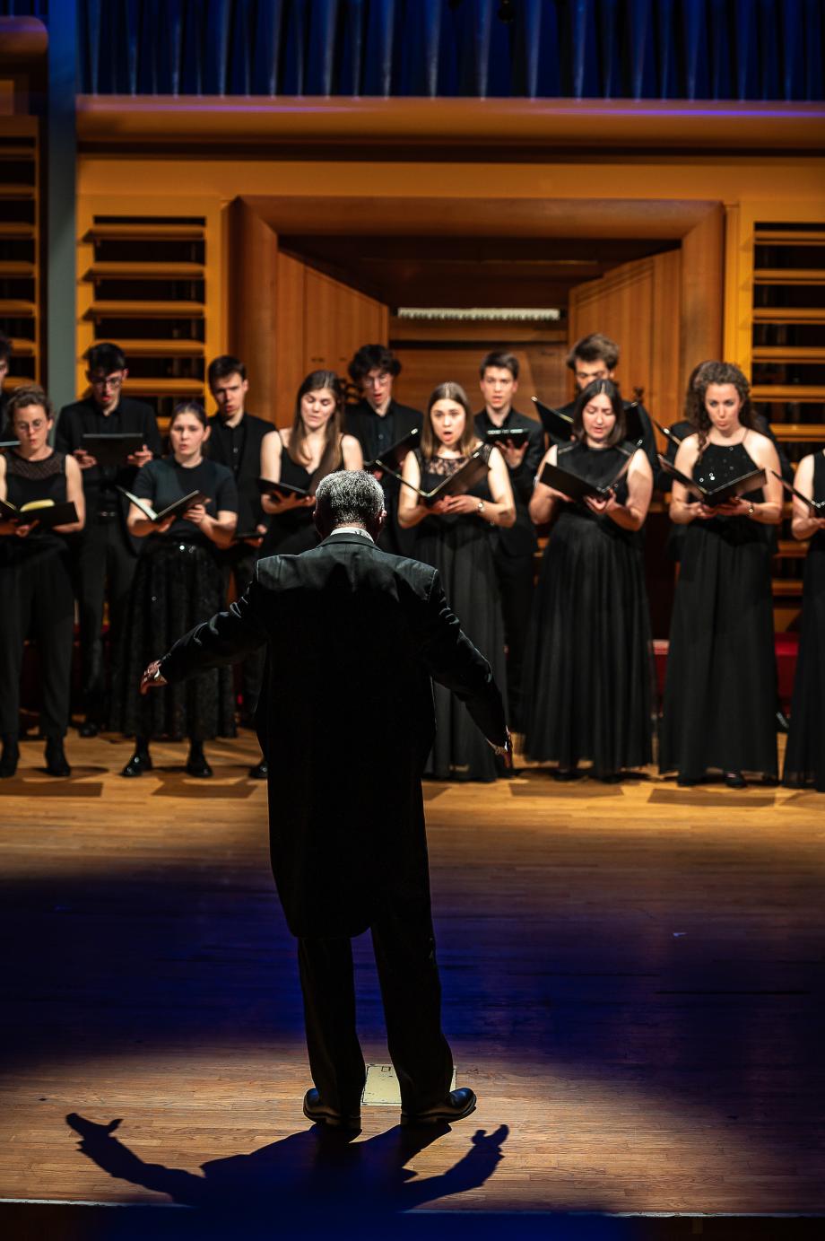 Prof. Denis Rouger dirigiert den Kammerchor im Konzertsaal. 