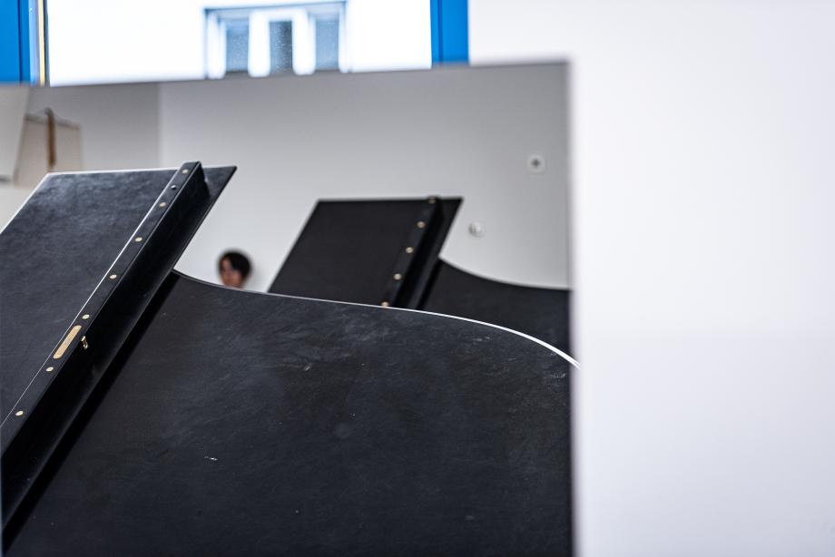 Detailaufnahme von zwei aufgeklappten Flügeldeckeln in eunem Unterrichtsraum. Im Hintergrund ist eine Studentin zu erkennen.