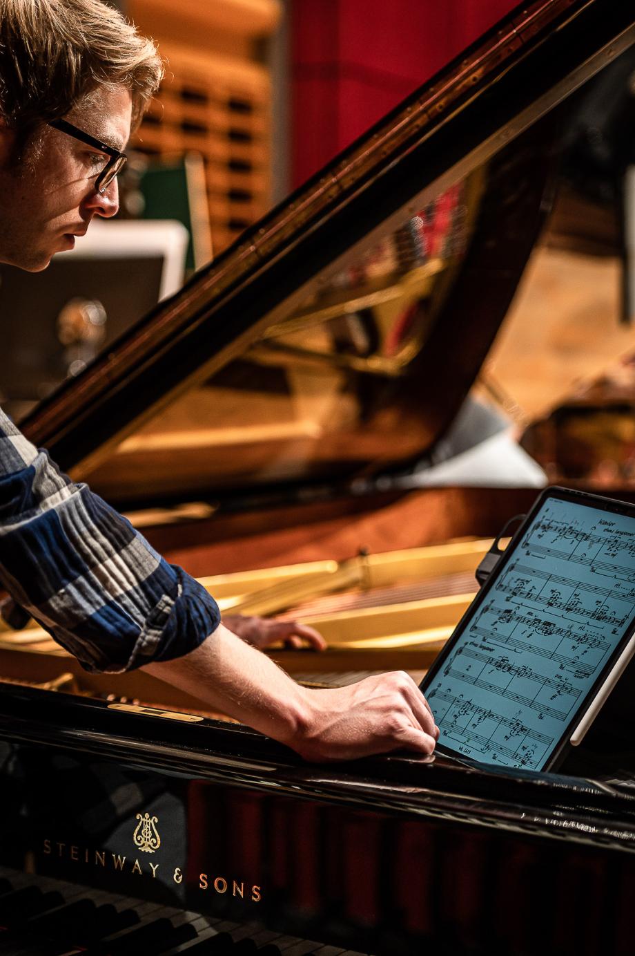 Der Pianist Alex Waite bei Proben im Konzertsaal. Sein Blick ist zum einen auf sein Tablet und auf den Resonanzraum des Flügels gerichtet.