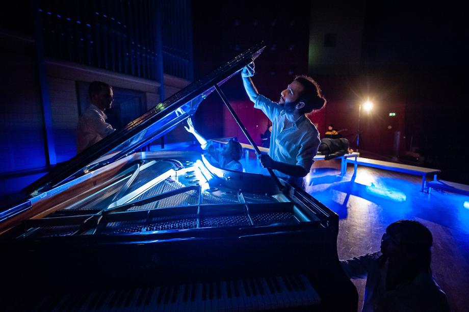 Der Konzertflügel wird von zwei Studierenden aufgeklappt und mit einer Hand angefasst. Die Szene findet in einer atmosphärisch blauen Installation statt.