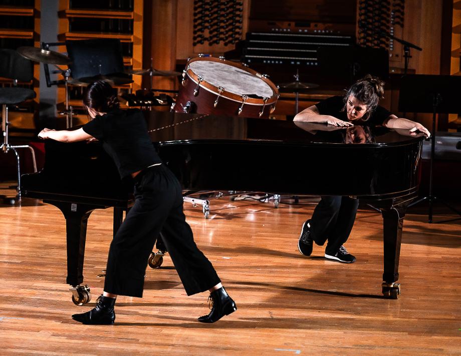 Zwei Studierende drehen im Rahmen einer performance den Flügel wie ein Kreisel. Sie umfassen mit weit ausgestreckten Armen den Flügelkorpus.