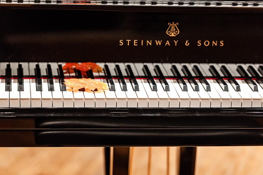 Auf der Klaviertastatur des Konzertflügels liegt im unteren Bereich der Tastatur ein gelb-orangenes Weinblatt.