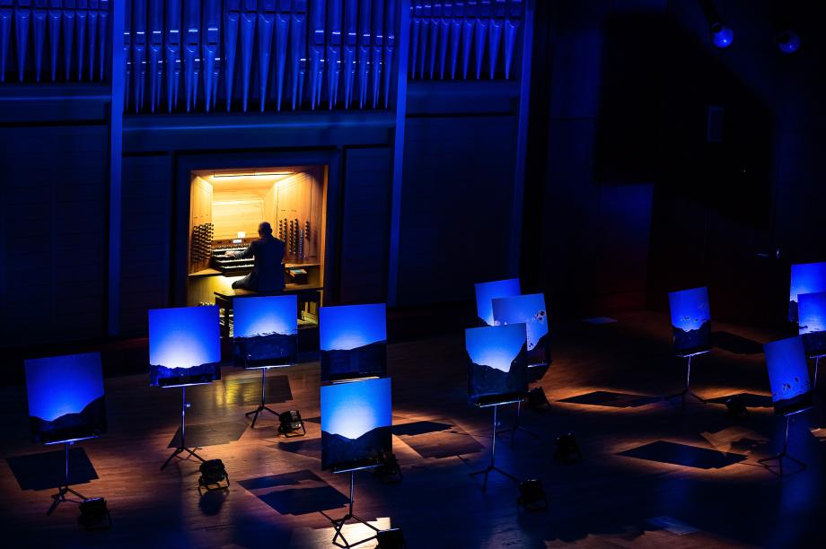 ORgelprofessor Jürgen Essl bei einem BLAU-Konzert. Auf dem Podium sind viele Fotografien von den Anden zu sehen, die individuelle blau beleuchtet werden.