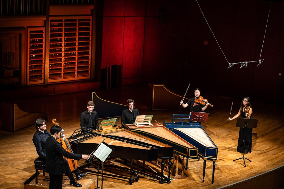 Seitlicher Blick auf die Konzertbühne. Vier Cembali stehen im Zentrum. Es musizieren Studierende der HMDK.