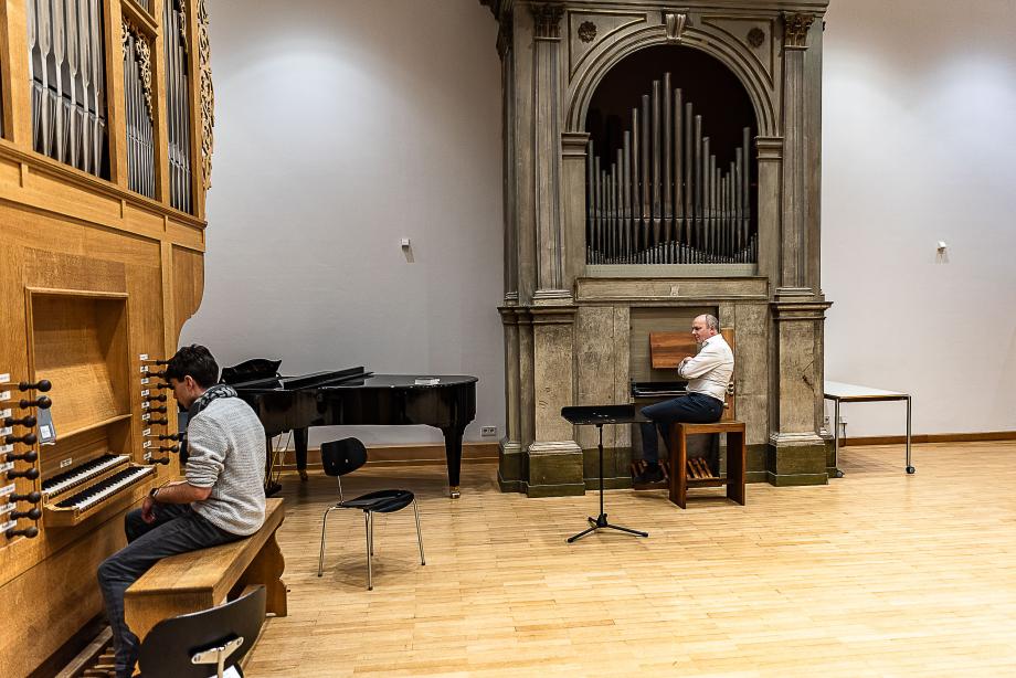 Unterrichtssituation mit Orgelprofessor Jürgen Essl und einem Studierenden. Der Studierende spielt an der Barock-Orgel, Jürgen Essl sitz auf der Bank der italienischen Orgel und gibt Anweisungen. In diesem Unterrichtsraum befinden sich drei Orgeln aus unterschiedlichen Epochen.
