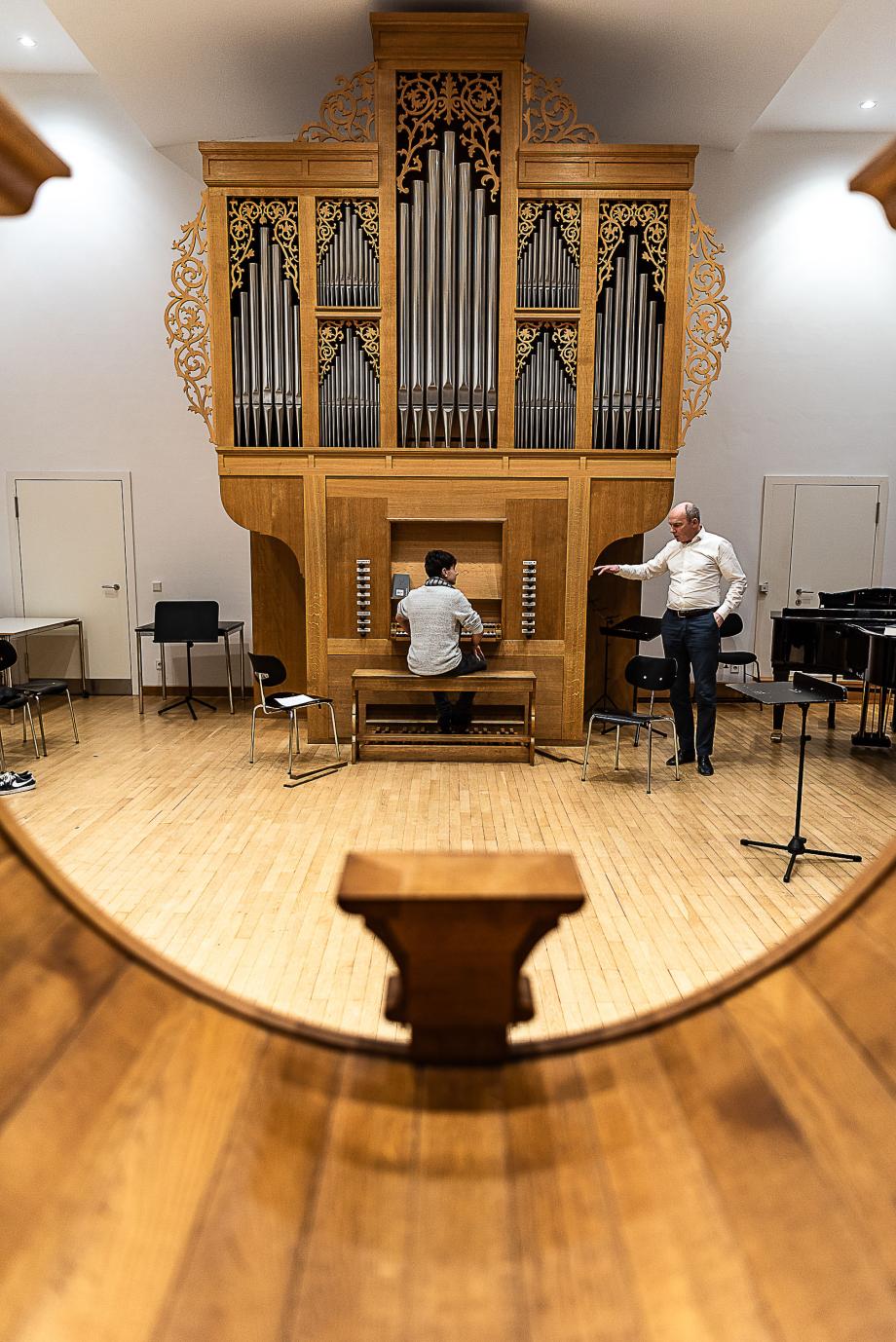 Blick aus der französischen Orgel auf die deutsche Barockorgel, wo Orgelprofessor Jürgen Essl gestikulierend einen Studierenden unterrichtet. In diesem Unterrichtsraum befinden sich drei Orgeln aus unterschiedlichen Epochen.