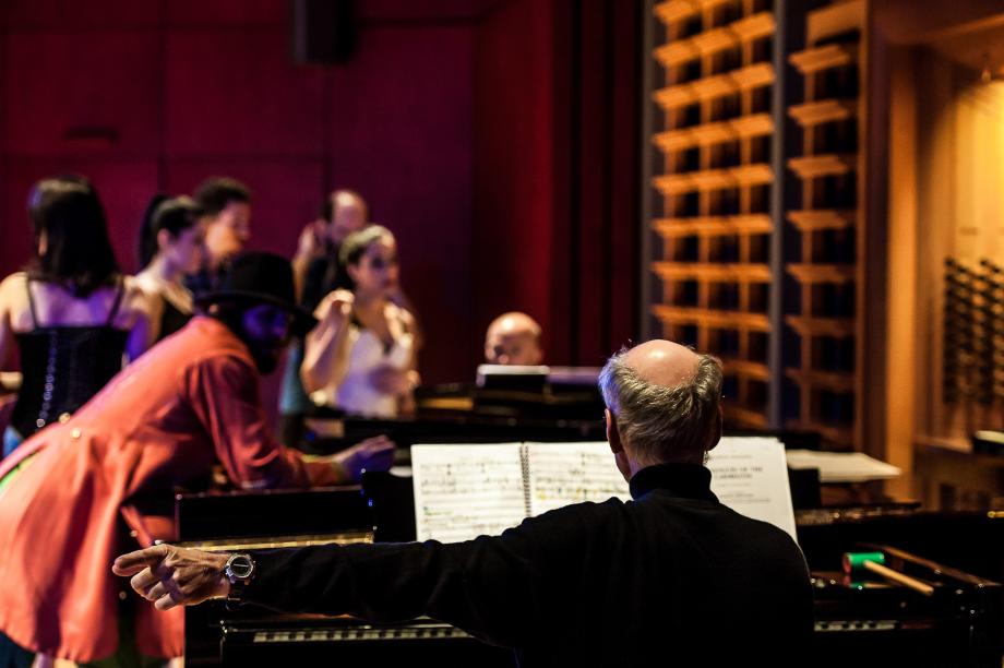 Szene aus dem Opernabend, wo sich Studierende um den musikalischen Leiter gruppieren. Aus der Rückenansicht des Pianisten aufgenommen.