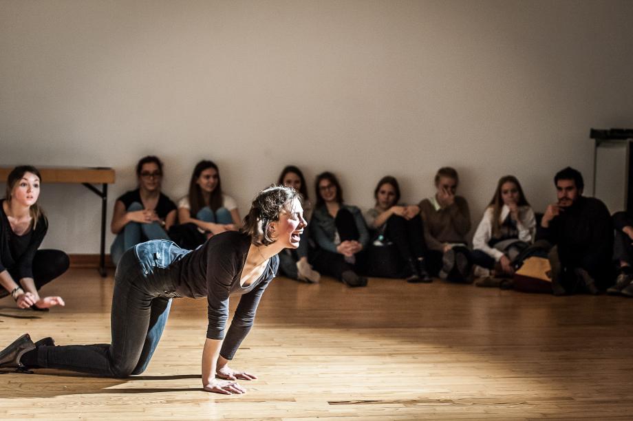 Auf allen Vierende spielende Studentin, die von der Seite beobachtet wird und den Fokus auf das Publikum hat.