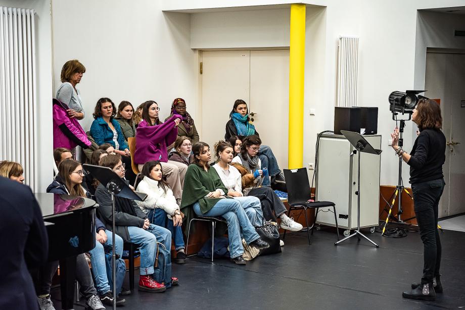 Prof.in Franziska Severin gibt eine Einführung in der Opernschule. Neugierig Interessierte, die im Opernstudio vor der Wand konzentriert stehen, verfolgen sie aufmerksam.