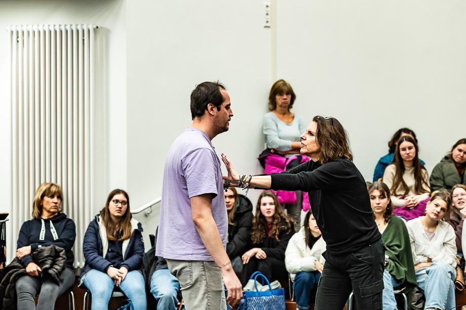 Szenische Arbeit von Franziska Severin mit einem Studierenden der Opernschule. Sie drängt den Studierenden mit ausgestreckten Armen von sich und wehrt ihn ab. Im Hintergrund beoachten Interessierte mit unterschiedlichen Gesichtsausdrücken die Situation.