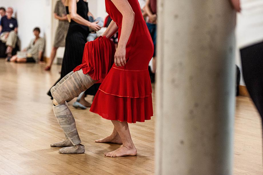 Es sind nur die Beine einer Studierenden zu sehen, die neben sich noch Beine einer großen Puppe autonom führt.