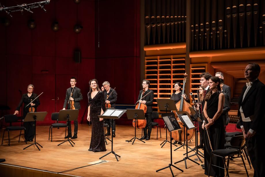 Prof.in Marion Eckstein beim Schlussapplaus mit einem Kammerensemble auf dem Konzertsaalpodium.